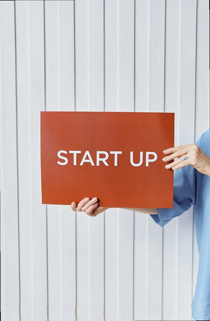 A person holding a sign reading 'START UP' against a white wooden backdrop.